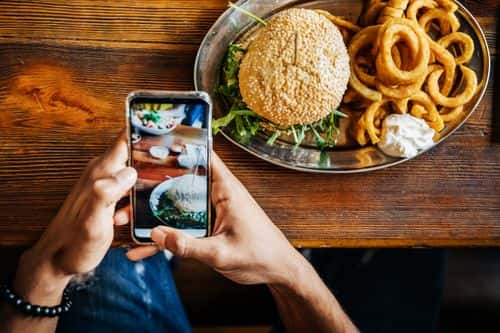 A man taking a picture of his artisanal burger with his smartphone before eating it.
Getty Images / 	Hinterhaus Productions