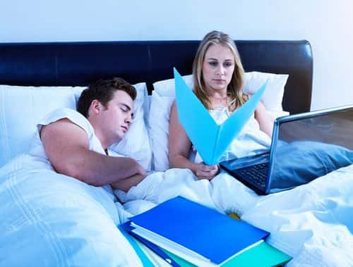 Woman working late in bed with laptop computer and paperwork as husband or boyfriend sleeps - stock photo - Getty Images | RapidEye