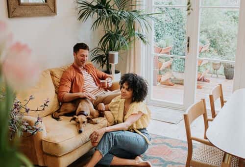 A young, interracial couple relax together in a living room with their lurcher dog - Getty Images | Catherine Falls Commercial