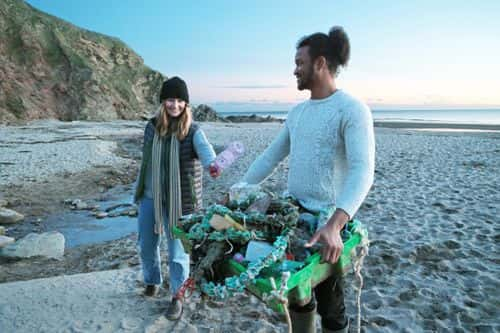 Mixed race couple cleaning rubbish off beach - Getty Images | Peter Cade
