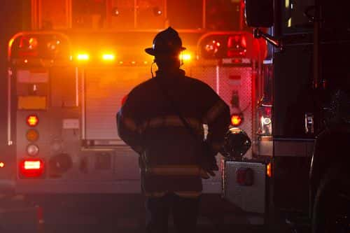 Firefighter silhouetted against a fire truck with flashing lights at an emergency scene. (Getty Images / Filo) 